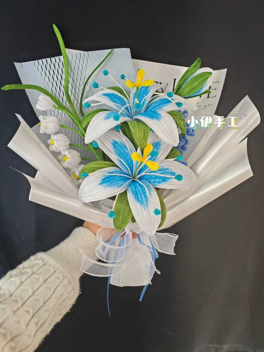 Hand holding a handmade Legend of Zelda Silent Princess pipe cleaner bouquet with blue and white gradient lily blooms, yellow stamens, teal berry accents, purple wisteria, lily of the valley, and green leaves wrapped in white paper with sheer organza ribbon