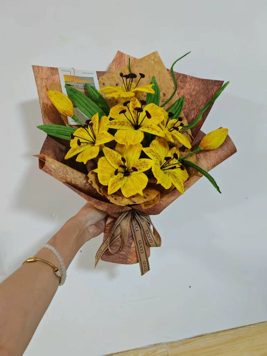 Hand holding a handmade yellow alstroemeria pipe cleaner bouquet with 6 chenille wire blooms, green twisted leaves, and kraft paper wrapping tied with a satin ribbon bow